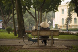 Person with a bicycle sitting on a bench in a park.