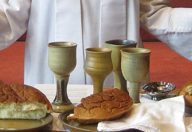Communion table set with 4 cups with a broken loaf of bread.