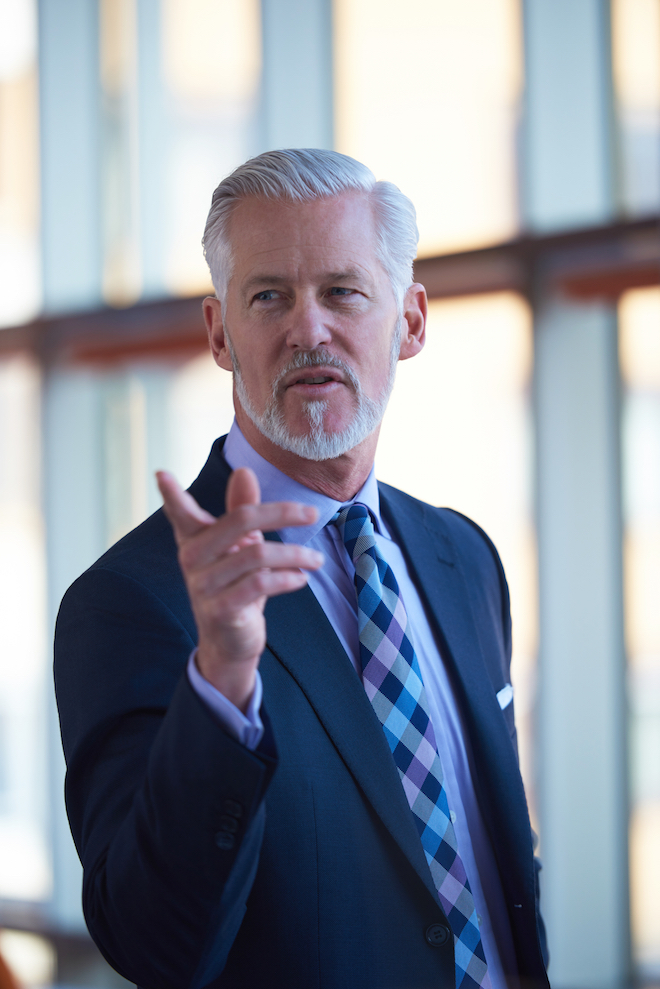 Photo of senior businessperson with grey beard and hair in a decisive stance