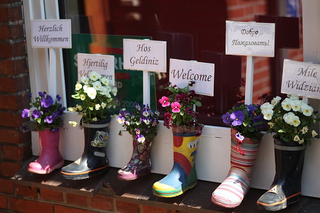 Flowers planted in rain boots with welcome signs in different languages.