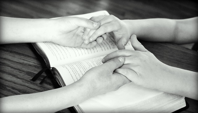 Hands held together in prayer over a Bible.