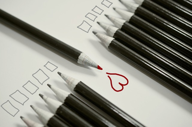 Black and white pencils in conformity except for one red color pencil facing the other way with a drawn heart.