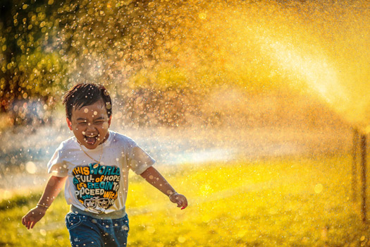 A child running through the sprinklers with delight.