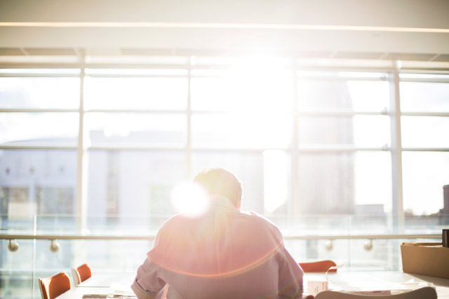 A person sitting in front of a large window with the sun streaming in.