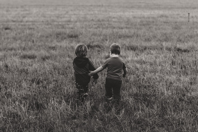 One child helping another as they walk in a field.