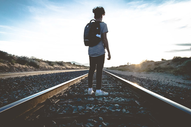 A man standing on train tracks looking to the sunrise.