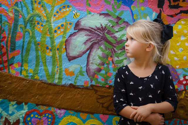 A little girl standing in front of a colorfully painted wall.