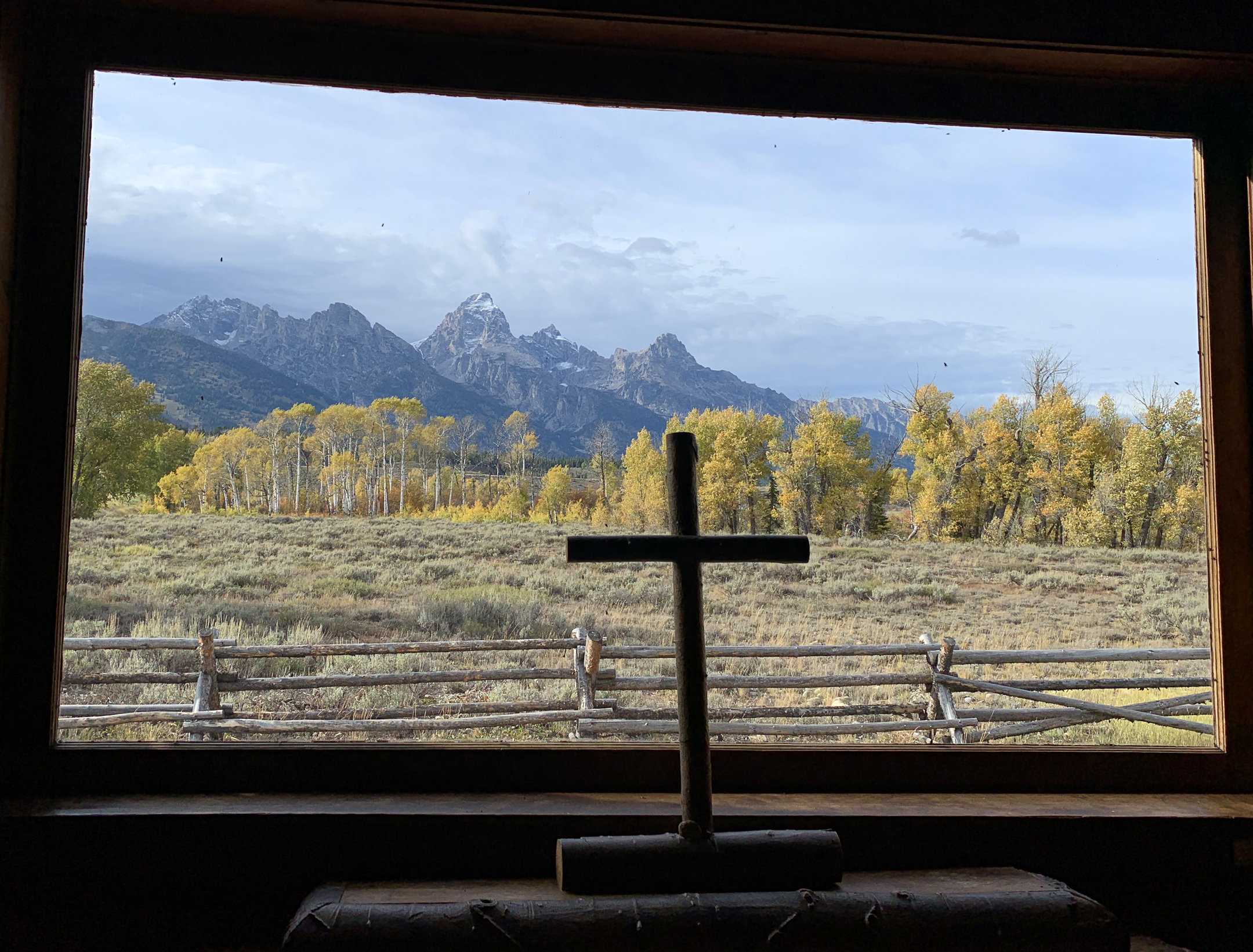 A cross in front of a window with the Grand Tetons seen through the window