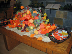 A communion table piled high with construction-paper pumpkins on whicb people have written things they are thankful for