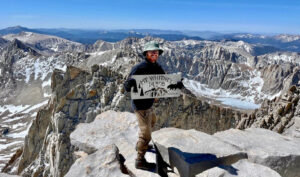 Mark's son Nathan standing on top of Mt. Whitney holding a sign reading "14,505 feet"