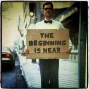 A man on a street corner with a sign that says "The Beginning is Near"